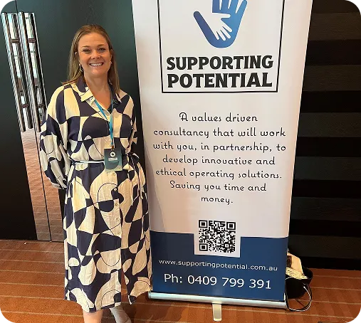 Angela beside a Supporting Potential pull-up banner at a conference